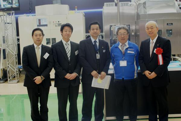 作業服姿の男性とスーツ姿の市長達4人が設備の前で記念撮影している写真